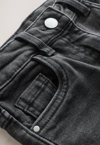 Schwarze Jeans aus Denim mit einem Design aus fünf Taschen, silbernen Knöpfen und einer strukturierten Oberfläche mit sichtbaren Nahtdetails.