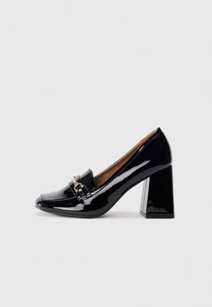 Black patent leather high-heeled shoe with a pointed toe and block heel. Features a decorative strap and buckle detail on the vamp.