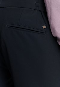 Zwarte broek met een slank ontwerp, zachte stoffen structuur, elastische tailleband, een discrete achterzak en een metalen accent met merklogo.