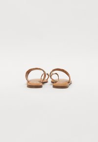 Sandales en cuir avec des brides multicolores tressées, semelles plates et design minimaliste. Elles présentent une texture lisse et un dos ouvert.