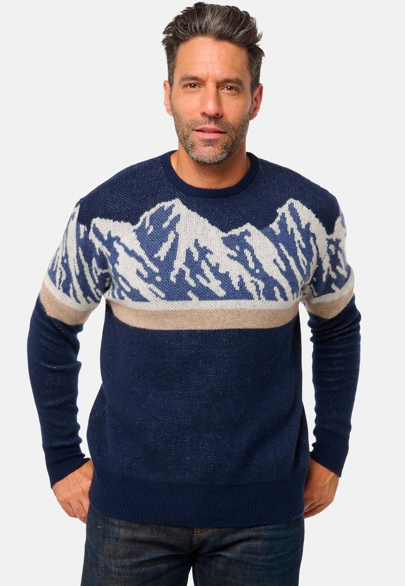 Pull tricoté en bleu marine avec un motif montagne en blanc et bleu, agrémenté d'une bande horizontale beige. Manches longues et ourlet côtelé.