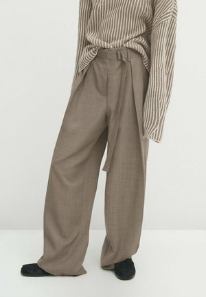 Beige wijde broek met stoffen riem, gedragen met een beige-wit gestreepte trui in de broek gestopt en zwarte schoenen.