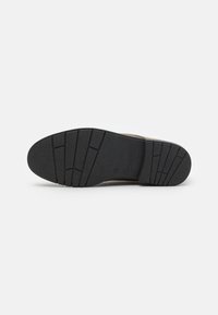 Suela de zapatilla con una superficie de goma negra texturizada y ranuras horizontales y verticales para tracción y agarre. El diseño es funcional.