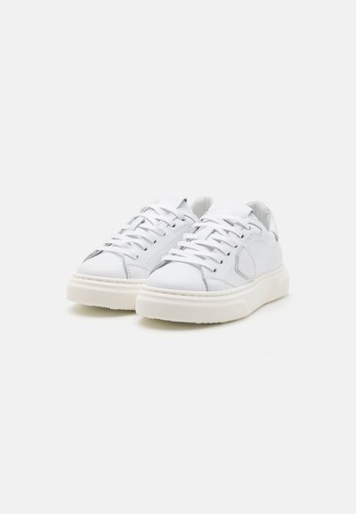 Sneakers en cuir blanc avec des accents texturés, des lacets plats et une semelle en caoutchouc crème. Bout arrondi et design minimaliste.