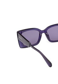 Ochelari de soare din plastic violet, cu lentile pătrate și un cadru gros. Temele sunt elegante și strălucitoare, având un detaliu subtil cu logo.