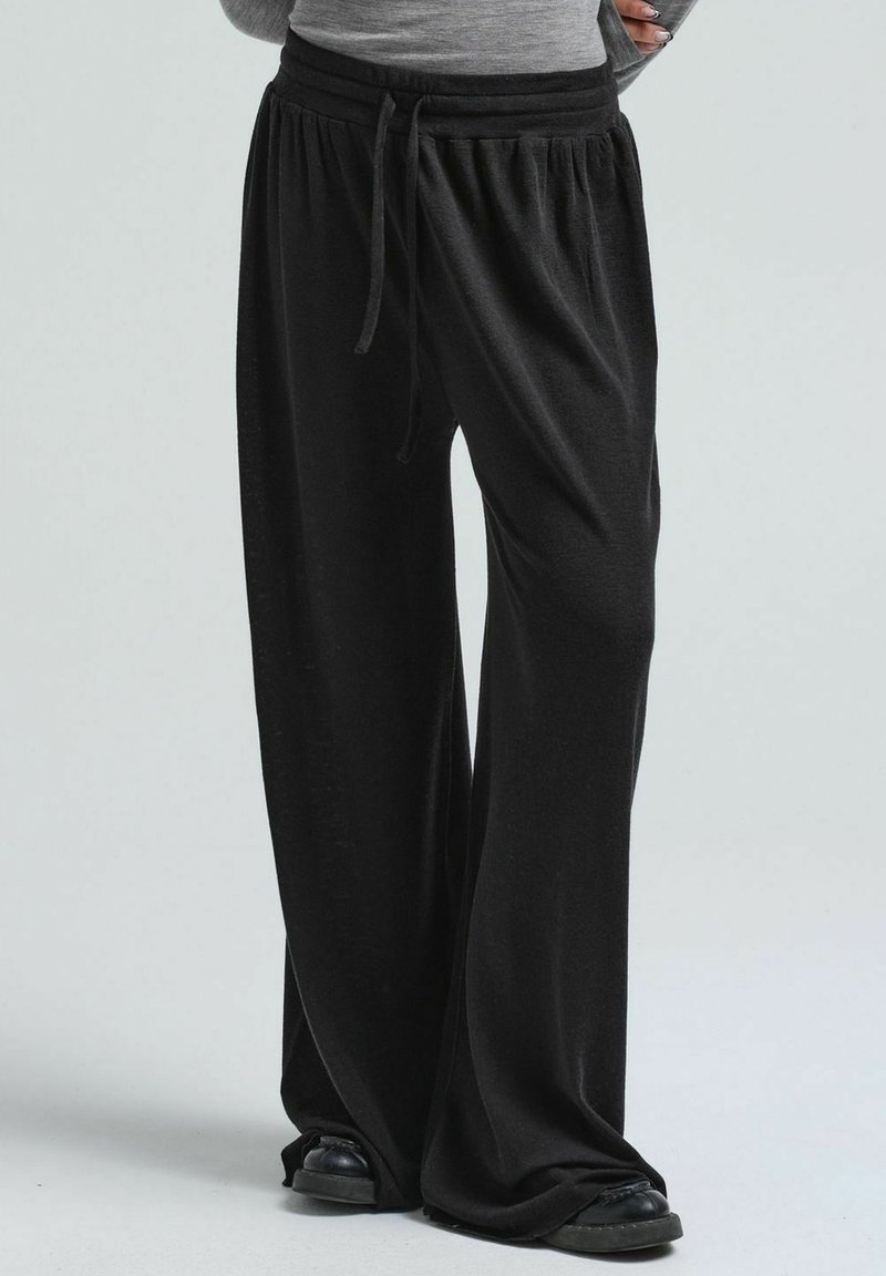 Schwarze weit geschnittene Hose aus weichem Stoff, mit einem elastischen Bund und einer Kordel, locker an den Knöcheln.