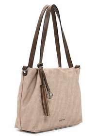 Sac en toile beige avec des poignées en cuir marron, des accessoires en métal argenté, et un pompon décoratif avec un charm en métal circulaire.