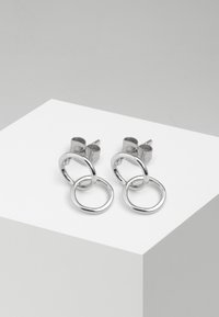 Orecchini a cerchio in argento con due design circolari collegati, finitura lucida, con chiusura a perno e superficie liscia.