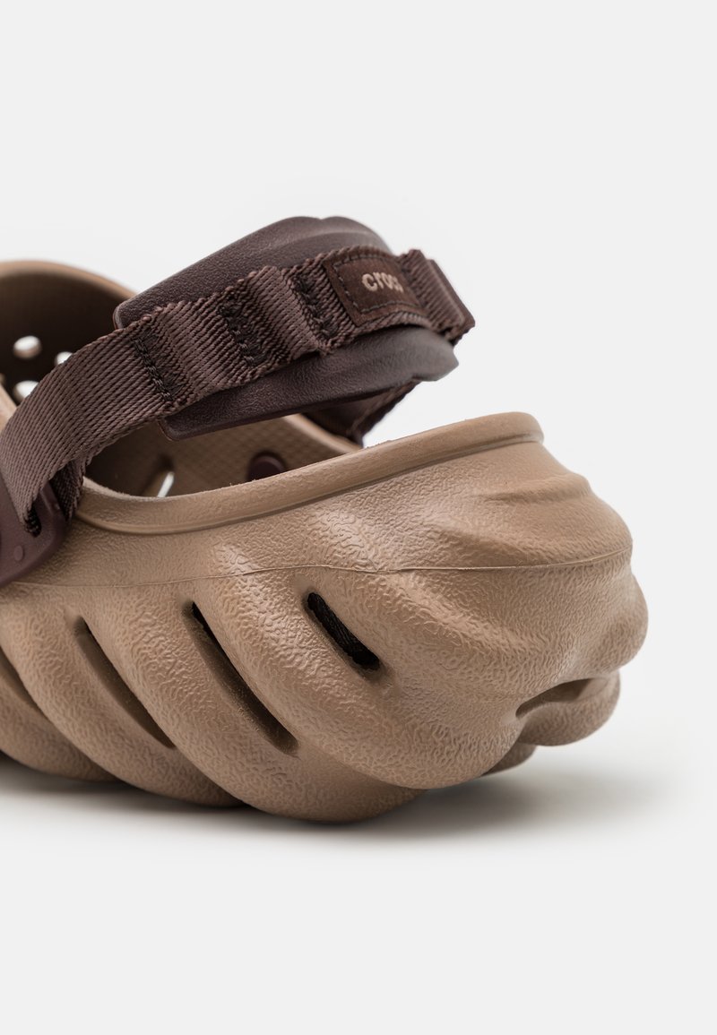 Sandalias marrones moldeadas con una superficie texturizada, laterales abiertos y una correa ajustable marrón para un ajuste seguro. Diseño de suela acanalada notable.