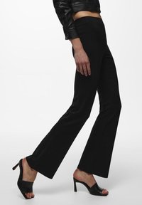 Zwarte flared broek van rekbare stof, met een hoge taille en een gladde textuur, gecombineerd met open-tipped zwarte hakken.