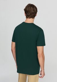 T-shirt in cotone verde scuro con maniche corte e colletto tondo, presenta un design semplice senza motivi o dettagli, modello che volta le spalle.