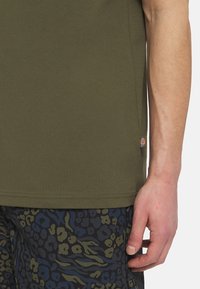 Olivgrön t-shirt med korta ärmar i bomull med en slät yta. Har en liten logotypetikett på sidan, i kombination med mönstrade shorts.