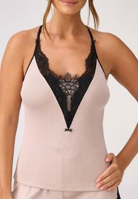 Żebrowany jasno beżowy top na ramiączkach z głębokim dekoltem V, zdobiony czarną koronką przy brzegach i ramiączkach, z małą czarną kokardką na środku.