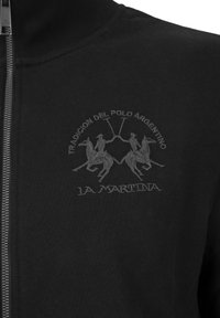 Zwarte ritssluitende jas met een gestructureerde stof, voorzien van een subtiele geborduurde logo van twee polo-spelers en de merknaam "La Martina."