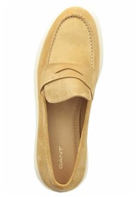 Tan suede slip-on shoe with a rounded toe, a front strap, beige inner lining, and white rubber sole. Features subtle stitching accents.