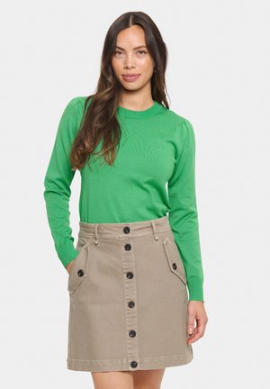 Groene geribbelde gebreide top met lange mouwen, gecombineerd met een beige A-lijn rok met frontzakken en zwarte knoopdetails.