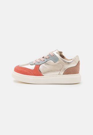 Lavtopet sneaker med metalisk guld læder, koral og brune ruskind aksenter, lyserøde snørebånd og en tyk hvid sål på en hvid baggrund.