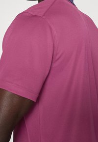 Koszulka polo z krótkim rękawem w różowym kolorze, wykonana z gładkiego materiału, z granatowym kołnierzykiem i eleganckimi przeszyciami.