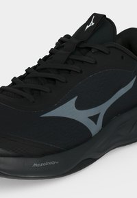 Μαύρο παπούτσι για τρέξιμο Mizuno με γκρι λογότυπο στο πλάι, μαύρα κορδόνια και παχύ παχουλό πέλμα με την ένδειξη Mizuno Energy NXT.