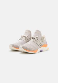 Scarpe da ginnastica beige chiaro con una tomaia in maglia traspirante, suola in gomma e accenti colorati in arancione e viola. Presentano lacci elastici.