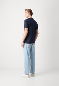Tricou bleu marin cu mâneci scurte, din bumbac, asociat cu blugi deschiși, cu croi lejer, și adidași albi cu accente bleumarin.