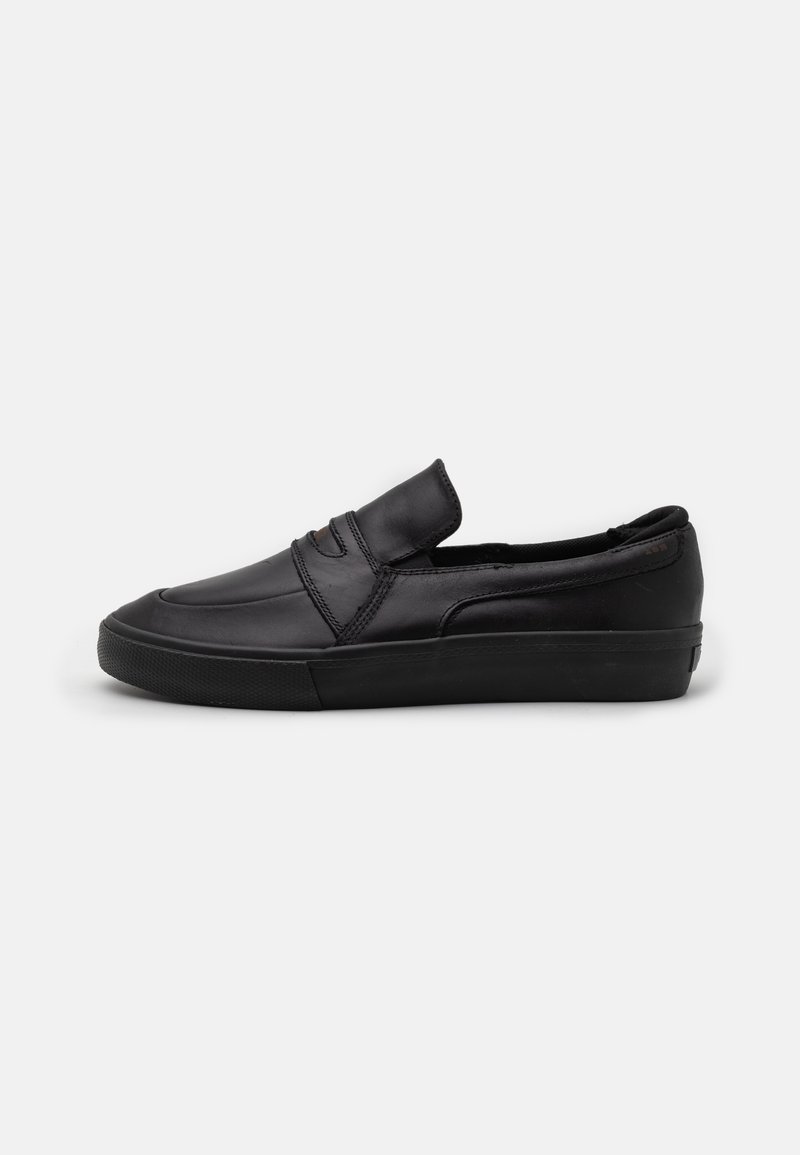 Svarta sko med slip-on design, tillverkade av slätt läder, med ett sömnadsdetalj på framsidan och en strukturerad gummisula för grepp.
