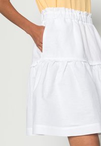 Bílá vícevrstvá sukně s elastickým pasem a bočními kapsami, vyrobená z lehkého materiálu s jemnou texturou.