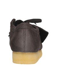 Zapato de ante negro con la parte trasera redondeada, que presenta una suela de goma amarilla y cordones negros. Costuras visibles a lo largo de la costura trasera.