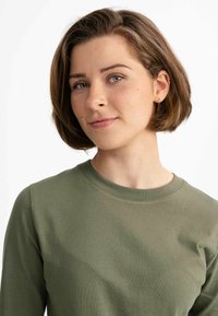 Olivgrünes Langarm-T-Shirt mit Rundhalsausschnitt. Weiches, glattes Material mit minimalen Nähdetails, locker um die Schultern geschnitten.