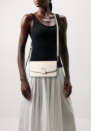 Crossbody bag in white leather with a smooth texture, gold hardware, and a flap closure. Features a prominent logo on the front.