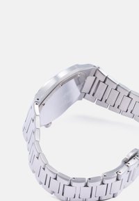 Reloj de acero inoxidable con caja octagonal, tono plateado, textura cepillada, diseño de pulsera de eslabones y herrajes de sujeción visibles.