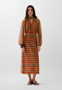Pitkähiha dress, jossa on korkea kaulus ja moniväriset raidat oranssissa, punaisessa ja keltaisessa. Rakenne-eläin ja pitkät puffihihat.