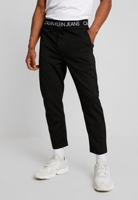 Svarta joggbyxor med dragsko i midjan och märkestyg i midjebandet. Tyget framstår som slätt med en avsmalnande bendesign.