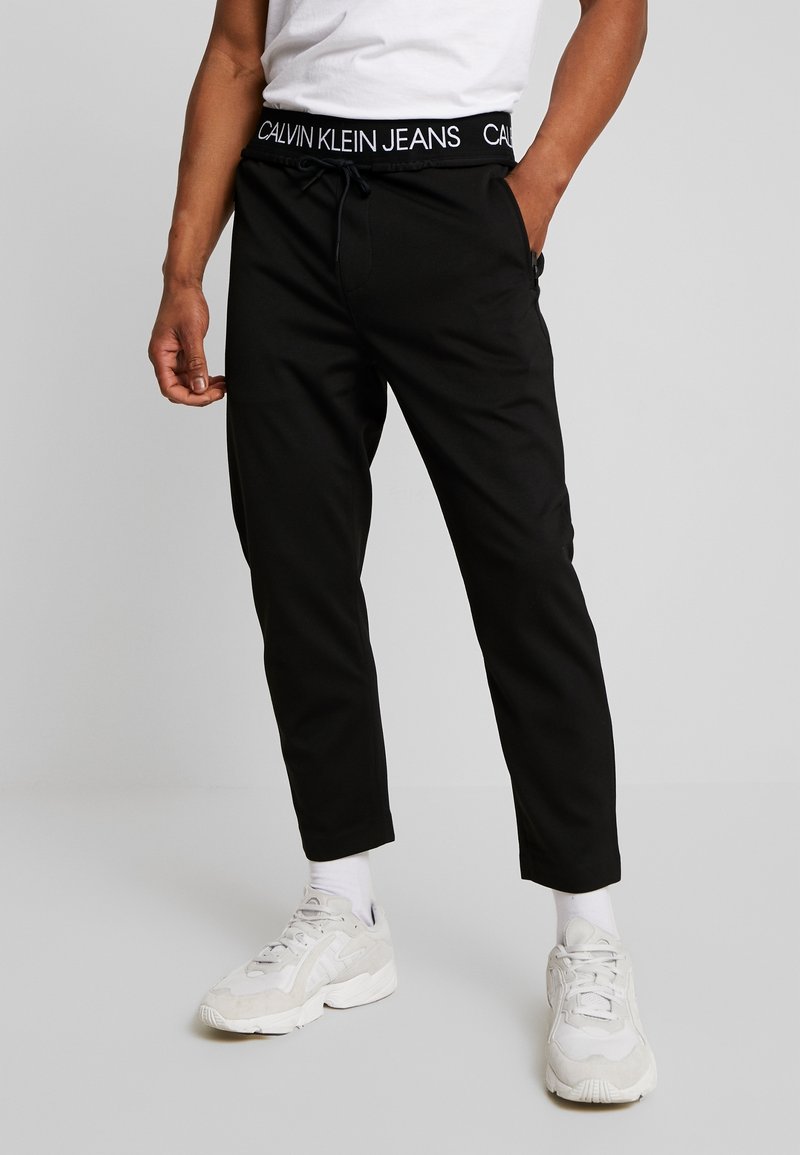 Svarta joggbyxor med dragsko i midjan och märkestyg i midjebandet. Tyget framstår som slätt med en avsmalnande bendesign.