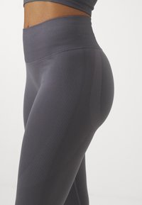 High-waisted, ribbed leggings in dark gray, featuring a smooth texture, fitted design, and accentuated seams for a streamlined look.