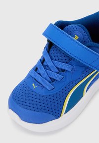 Μπλε αθλητικό παπούτσι παιδικό με επάνω μέρος από δίχτυ, κίτρινο λογότυπο Puma, λευκή σόλα, μπλε κορδόνια και μπλε λουρί με Velcro στην κορυφή.