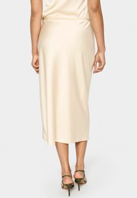 Beige Satin-Midi-Rock mit glatter Textur, im Slip-On-Design und seitlichem Schlitz, kombiniert mit grünen Riemchen-Heels.