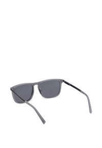 Lunettes de soleil rectangulaires grises avec des verres teintés foncés et des branches fines et translucides grises, vues légèrement de derrière sur fond blanc.