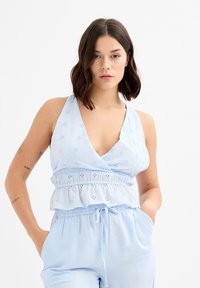 Top sin mangas de color azul claro con un escote en V profundo, bordado de ojetes y dobladillo con volantes. Confeccionado en una tela suave, con un ajuste relajado.