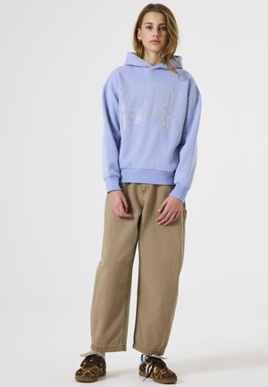 Lichtblauwe hoodie met zilveren bedrukking, gecombineerd met beige wijde broek en sneakers met luipaardprint. Casual katoenmix stof.