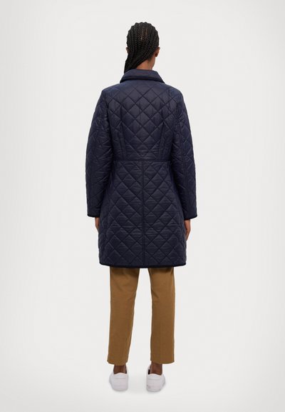 Jūras spēku krāsas klātne garais mētelis ar pielāgotu apkakli, kas piedāvā piegriezuma jostasvietu, sānu kabatas un teksturētu virsmu. Saskaņots ar gaiši brūnām biksēm.