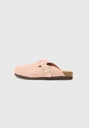Sabot en daim rose à enfiler avec boucle dorée, semelle intérieure en liège et semelle extérieure texturée marron foncé, présenté de profil sur un fond uni.