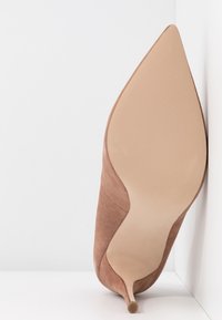 Chaussure à talon haut en daim marron avec bout pointu, semelle beige lisse et accents texturés sur la tige. Design à talon stiletto.