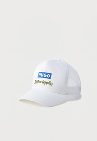 Gorra de béisbol blanca con visera curva, presenta un logo azul "HUGO" y el texto "Jujutsu Kaisen" en verde. Laterales de malla para mayor transpirabilidad.