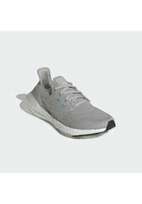 Scarpa sportiva grigio chiaro con parte superiore in mesh, dettagli in plastica, una suola spessa e imbottita, e una punta arrotondata; presenta dettagli testurizzati sui lati.