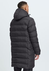 Abrigo largo acolchado negro con capucha, que presenta un diseño acolchado, textura suave y cordón ajustable. De longitud completa y de manga larga.