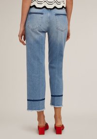 Vaqueros de mezclilla azul claro con pierna recta, dobladillo deshilachado y rayas de acento azul oscuro en los puños. Los bolsillos traseros son visibles.