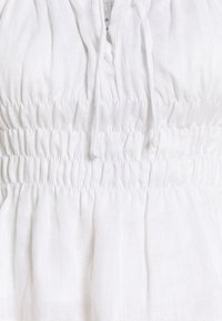 Bílá lehká tkanina se shromážděným elastickým smockováním a zavazovací šňůrou v pase oděvu.