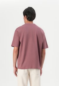 T-shirt s kratkimi rokavi in okroglim ovratnikom v barvi prašne vrtnice, izdelan iz mehkega materiala z udobnim krojem in minimalnimi šiviljskimi detajli.