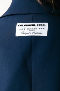 Granatowy element odzieżowy z białą metką z napisem "COLOURFUL REBEL", zawierający tekst o marce oraz informację "Zaprojektowane w Amsterdamie."